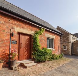 A brick cottage entrance with plants in pots and a wooden door at Mayfield Cottage in Nr Malmesbury