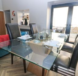 A dining area with a glass table set with plates glasses and cutlery surrounded by black chairs near glass patio doors at Mayfield Cottage Nr Malmesbury