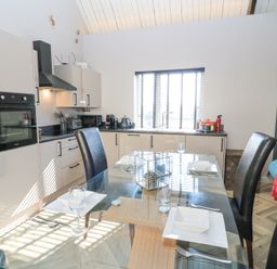A kitchen with glass dining table set for four and modern appliances at Mayfield Cottage Nr Malmesbury