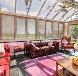A conservatory with red leather sofas armchair wooden tables and a fruit bowl at The Old Forge Cottage in Kilkhampton