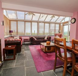 A living room with leather sofas wooden coffee table and dining chairs at The Old Forge Cottage in Kilkhampton