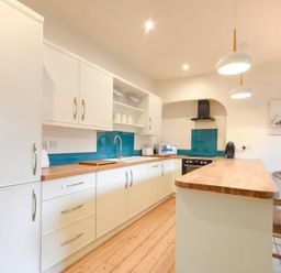 A kitchen with white cabinets wooden countertops blue backsplash and wooden bar stools at The Loft (Amble) in Amble
