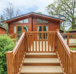 A wooden cabin with a deck and stairs surrounded by trees and bushes at 8 Waterside Wood White Cross Bay near Troutbeck Bridge