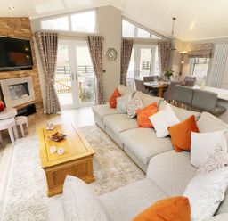 A living room with a large sectional sofa and wooden coffee table near a dining area at 8 Waterside Wood White Cross Bay near Troutbeck Bridge