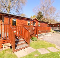 A wooden lodge with a deck and stairs in a grassy area at Bowness 66 in Troutbeck Bridge