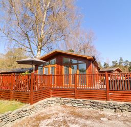 A wooden chalet with a fenced deck and umbrella on a sunny day at Bowness 66 in Troutbeck Bridge