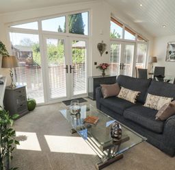 A living room with a dark sofa glass coffee table tall windows and dining area at Bowness 66 in Troutbeck Bridge
