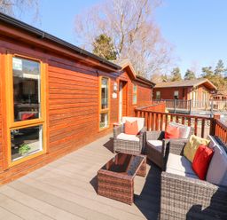 An outdoor deck with wicker seating and cushions outside wooden lodges at Bowness 66 in Troutbeck Bridge