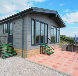 A small house with stairs leading to two doors and a patio with outdoor furniture and an umbrella at Midway Lodge in Cawsand near Kingsand
