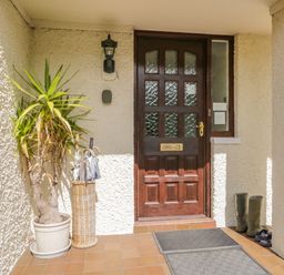An entrance door with glass panels flanked by a potted plant an umbrella stand with umbrellas and a pair of boots at Brantfell Lodge in Bowness-On-Windermere