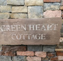 A stone plaque with the words Green Heart Cottage mounted on a multicolored stone wall at Greenheart Cottage in Pontrhydyfen