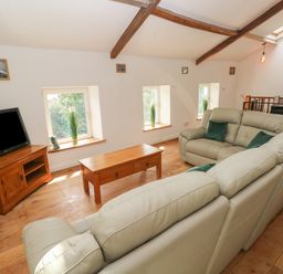 A living room with cream sofas a wooden coffee table a television on a wooden stand and windows on a slanted wall at Greenheart Cottage in Pontrhydyfen