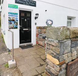 Front entrance with black door stone wall and holiday let sign at Greenheart Cottage in Pontrhydyfen