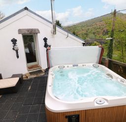 An outdoor patio area with a hot tub and outdoor seating next to a white building at Greenheart Cottage in Pontrhydyfen