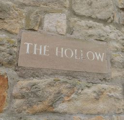 A stone wall with a plaque reading the hollow at The Hollow in West Woodburn