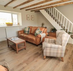 A living room with a brown leather sofa two green pillows a checkered armchair wooden coffee table and staircase at The Hollow in West Woodburn