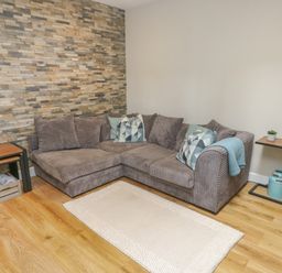 A corner sofa with cushions and a rug on a wooden floor next to two side tables in a living room at Fir Tree Cottage in Llanrug