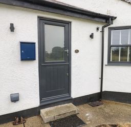 An exterior door with a glass panel next to a blue mailbox and window with blinds at Bay Tree Cottage in Llanrug