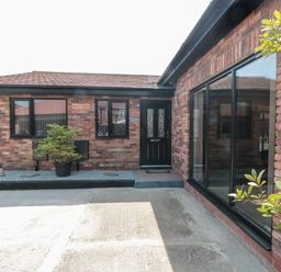 Exterior view of a brick house with a black front door windows a potted plant and a concrete driveway at 31A The Green in Scalby