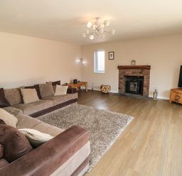 A living room with a brown sectional sofa a rug a brick fireplace and a television on a wooden stand at 31A The Green in Scalby