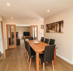 A dining room with a wooden table and eight black chairs near a living room at 31A The Green in Scalby