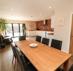 A dining area with wooden table and black chairs next to a kitchen with white cabinets and a brick backsplash at 31A The Green in Scalby