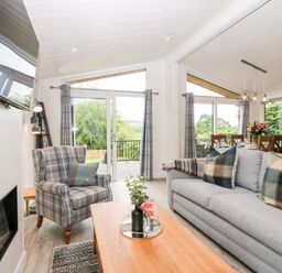 A living room and dining area with a gray sofa and checkered armchair at Eden Fields Lodge in Cupar Fife
