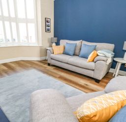 A living room with gray sofas blue and yellow cushions a round side table with a lamp and a light blue rug at Leos Place in Weymouth