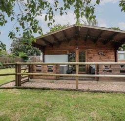 A wooden cabin with a fenced porch and garden at Pigsfoot Lodge in Ash Thomas near Halberton Devon
