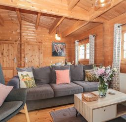 A wooden living room with a gray sofa and armchair a coffee table with flowers and a painting on the wall at Pigsfoot Lodge in Ash Thomas near Halberton Devon