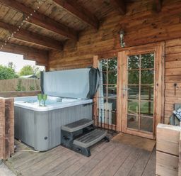 A porch area with a hot tub steps glass doors and wooden walls at Pigsfoot Lodge in Ash Thomas near Halberton Devon