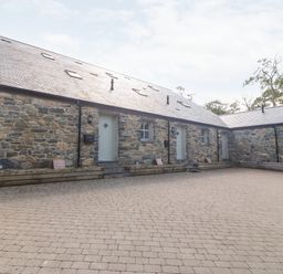 A stone building with multiple doors and windows and a paved courtyard at 3 Pensyflog Barns in Porthmadog