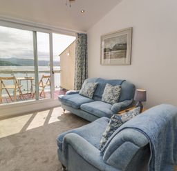 A living room with blue sofas and a TV next to a balcony with outdoor chairs at 25 South Snowdon Wharf in Porthmadog