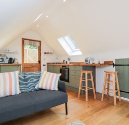 A kitchen area with green cabinets wooden countertops two wooden stools sofa with striped pillows and a wooden floor at The Rookery in Fulbrook near Burford