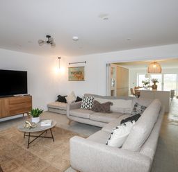 A living room with two sofas a coffee table a TV on a wooden stand and a visible kitchen in the background at Ysgol Fawr Big School in Benllech