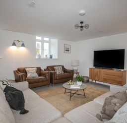A living room with two brown armchairs two gray sofas a round coffee table and a wooden TV stand at Ysgol Fawr (Big School) in Benllech