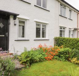 A row of white houses with black doors and windows and a garden with green grass flowers and bushes at 1 Millbank in Keswick