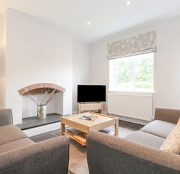 A living room with two sofas a coffee table a small television and a decorative fireplace at 1 Millbank in Keswick