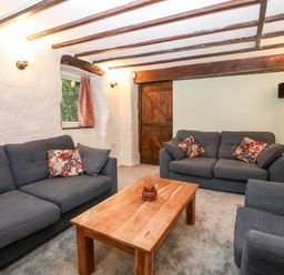 A living room with two sofas an armchair a wooden coffee table a floor lamp and wooden beams at Is Y Graig in Beddgelert