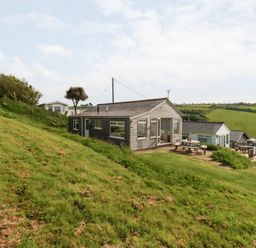A wooden chalet on a grassy hillside with picnic tables and other chalets in the background at Siesta Chalet Eype Mouth Chalet Park