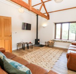 A living room with leather sofas a rug wood stove and large window at The Barnhouse Felmingham near North Walsham