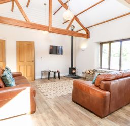 A living room with two brown leather sofas a wood stove a rug and exposed wooden beams at The Barnhouse in Felmingham near North Walsham