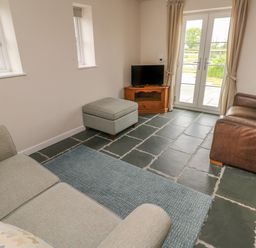 A living room with sofas ottoman television and glass doors at Ystabl Robyn in Llanddarog