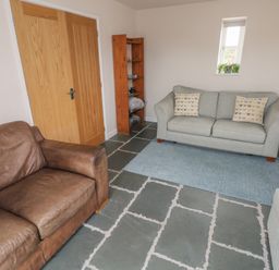 A living room with two sofas a blue rug a wooden shelf a small blue side table and a standing lamp at Ystabl Robyn in Llanddarog