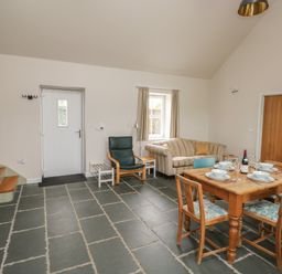A dining area with a wooden table set for four, a striped sofa, an armchair, and stairs in a room at Ystabl Robyn in Llanddarog