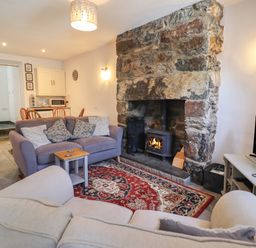 A living room with two sofas a stone fireplace and a dining area at Llygoden Cottage in Beddgelert