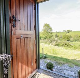 An open wooden door leading to a grassy field and trees at Puddle Duck Shepherds Hut in Crackington Haven