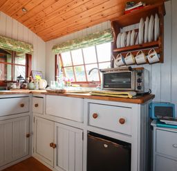 A kitchen corner with cabinets a countertop toaster oven and a wooden plate rack at Puddle Duck Shepherds Hut in Crackington Haven