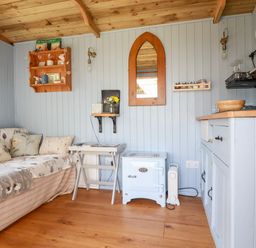 A small living space with a couch, a side table, a stove, a mirror, shelves, and kitchen cabinets at Shepherds Retreat in Maxworthy near Crackington Haven