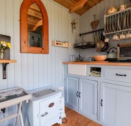 A small kitchen with blue cabinetry a wooden countertop a toaster oven a kettle hanging pots and cups and a small stove at Shepherds Retreat Maxworthy near Crackington Haven